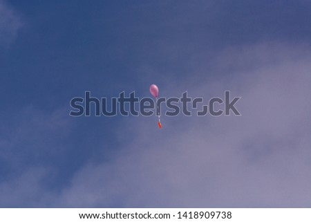 Pink balloon with ribbon and greeting card in front of blue sky