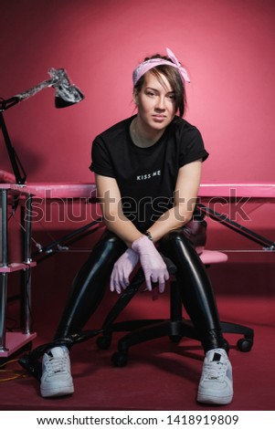 Portrait of a professional tattoo master woman. Black clothes, and dreadlocks. Red, pink and white background. Place of work tattoo master. Tattoo salon for lesbians.