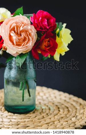 Coloful roses in vase on a wicker napkin on black background