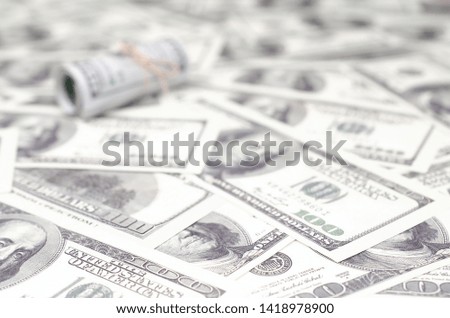 US dollars rolled up and tightened with band lies on a lot of american banknotes with blurred background