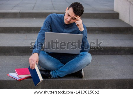 Perplexes student preparing for an exam in campus area sitting on university stairs. Student man with laptop, sitting on university stairs. Technology, communication, education and working concept.