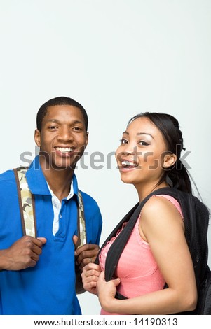 Two students wearing backpacks look at the camera and smile. Vertically framed photograph