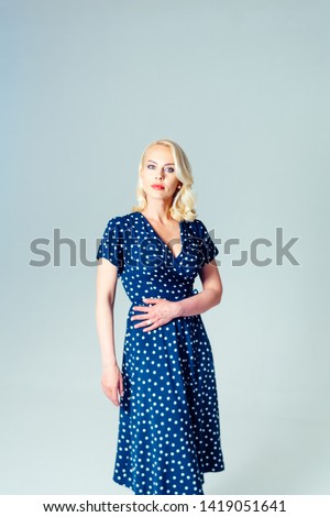 Studio portrait of beautiful blonde woman in a dark blue dress against white plain background