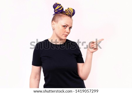 Young woman points her finger to the side, showing something to side empty copy space, concept girl advertisement product. The woman has dreadlocks on her head, freckles on her face. White background.
