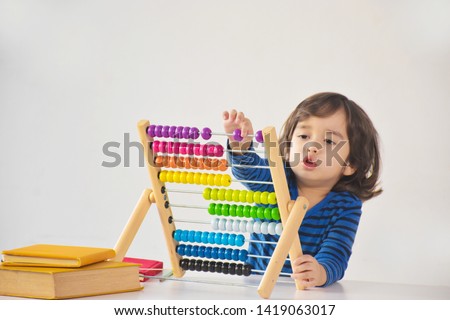 A young cute handsome asian caucasian boy is using the abacus with coloured beads to learn how to count in class - white background and copy space. Royalty-Free Stock Photo #1419063017