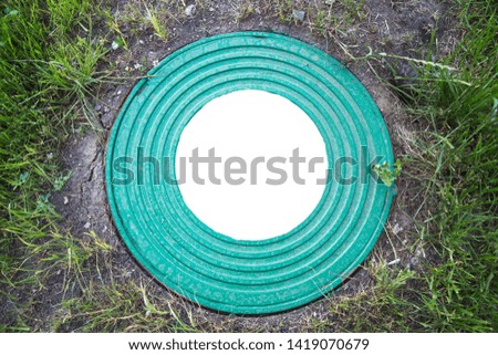 Hatch well cast iron heavy turquoise with a pattern of many rings on a background of green grass. In the center of the round white background for photo inscription