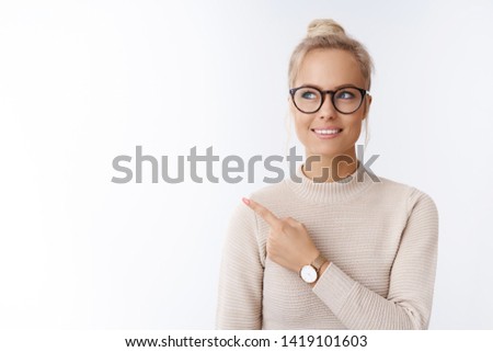 Closed-up shot of beautiful caucasian blond woman in glasses and sweater feeling creative and productive pointing at upper left corner smiling dreaming, thinking against white background
