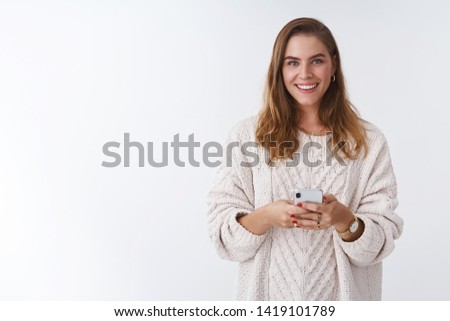 Studio shot charming happy smiling woman holding smartphone looking camera positive grinning communicating using app featurused. Female blogger posting pic online smm working via phone