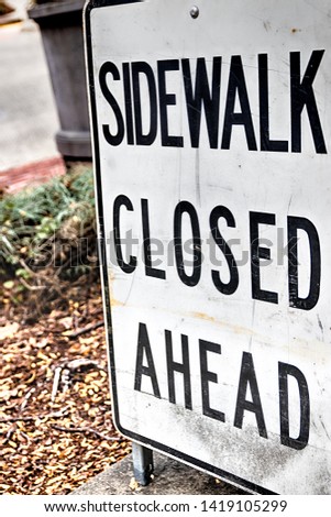 Abstract sidewalk closed ahead sign with plants in the distance