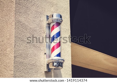 A view of a barber's pole on the side of a local barber shop building.