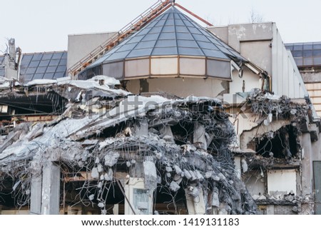 Photo of destroyed building, protruding reinforcement. Demolition of a building, house ruins, reconstruction, bricks and metal. Dismantling of structure.Heavy machinery, bulldozer, excavator-destroyer