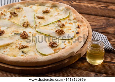 Traditional pizza with pear, nuts and blue cheese on a wooden background. Close up. Top view.Pear pizza on wooden board on a light background. Top view