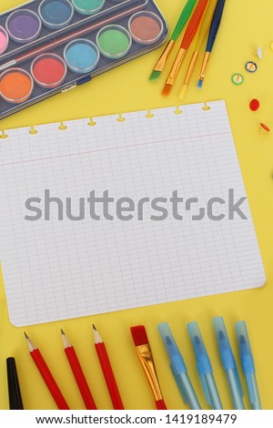sheet from school notebook and colored various stationery. Back to school concept, top view, paints, pencils, pens, copy space, vertical