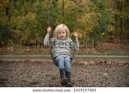 Cute blond female child on a swing in autumn