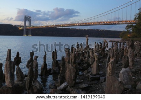Sisyphus Stones stacked at the banks of the Hudson River in Fort Washington Park at sunset with George Washington Bridge in the background, New York                        