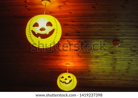 A bright orange pumpkin lamp is hanging off the wall a house during Halloween season