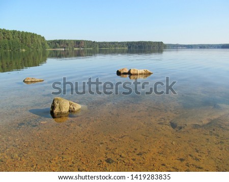 Summer idyllic landscape with beautiful lake. Calm transparent water surface with stones and sandy bottom on a bright quiet day. Harmony and pacification of nature - a beautiful concept for wallpaper.
