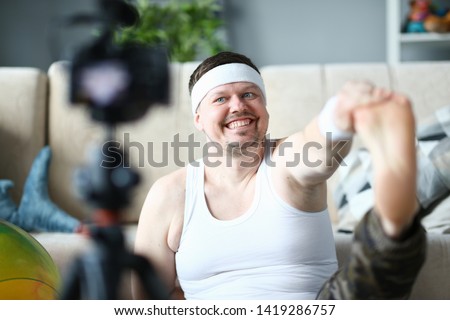 Happy Vlogger Record Stretching Exercise on Camera. Bearded Man Shooting Aerobic Warmup for Leg on Digital Camcorder for Sport Vlog. Male Doing Gymnastics in Apartment. Healthy Lifestyle Photo