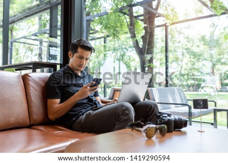 Asian man using gadgets Inspired, Confident young man working on laptop while sitting at his working place in coffee shop, Freelance work concept.