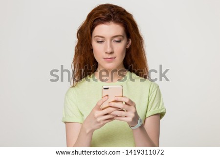 Head shot on grey white wall red-haired female holding smart phone wireless gadget reading message chatting online browse internet media news, electronic devices overuse, shopping in internet concept