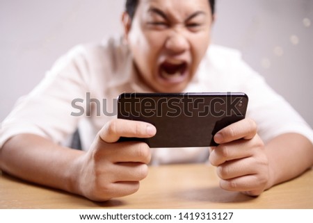 Photo image portrait of a cute handsome young Asian man with funny face playing games on tablet, sad angry loosing expression