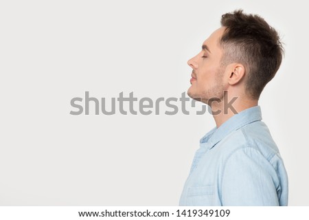 Side profile view man standing on grey background aside empty copy space for your advertisement text. Male in blue shirt closed eyes enjoy fresh air dreaming or positive powerful affirmations concept