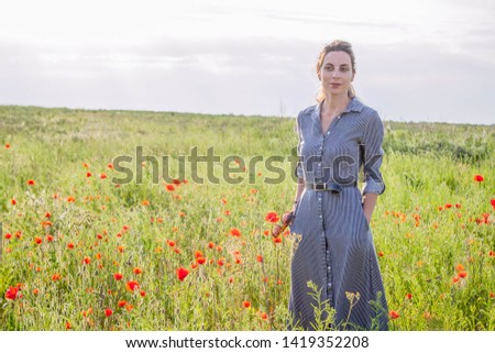 Dreamy woman in blue striped dress is standing in a beautiful herb flowering poppy field