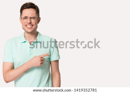 Confused man pointing finger aside at copy free space looking at camera show something awkward and strange pose isolated on grey white background, shameful uncomfortable embarrassing situation concept Royalty-Free Stock Photo #1419352781