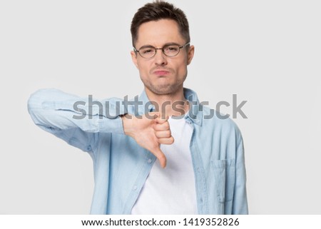 Man wearing glasses jean shirt looks at camera show thumbs down dissatisfied face expression studio head shot on grey background, dislike negative feedback, disagreement disapproval rejection concept