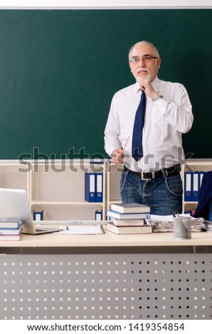Aged male teacher in front of chalkboard 
