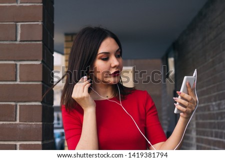 beautiful young woman with red lipstick in red dress uses phone and earphones