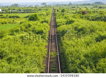 Aerial top view of the rusty rails crossing the green field in a summer day. Aerial view of railway track through countryside, drone top view pov of rails as abstract background