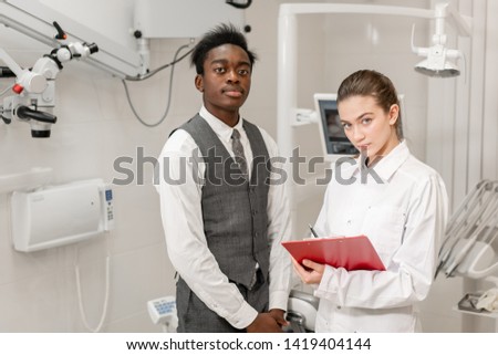 Young Woman dentist makes a diagnosis and records recommendations. African male patient in dental clinic. Medicine, health, stomatology concept. dentist treating a patient.