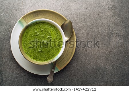 Spring healthy food. Green creamy soup with vegetables and herbs on gray background