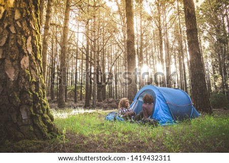 Couple of young trendy women drinking coffee and tea sitting in a camping tent Trendy sporty girls relaxing in the forest after an hiking holiday Tourism adventure active lifestyle and healthy concept