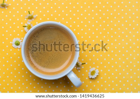 Chamomile flowers and a cup of coffee on a yellow polka dot background. Good morning.