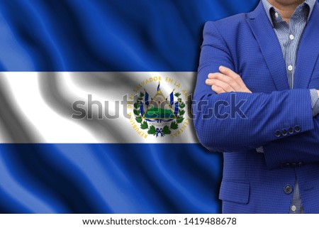 The concept of business, government, power. The elite of the country. Copy space or text. Man in blue suit close-up against the background of the developing flag of El Salvador.