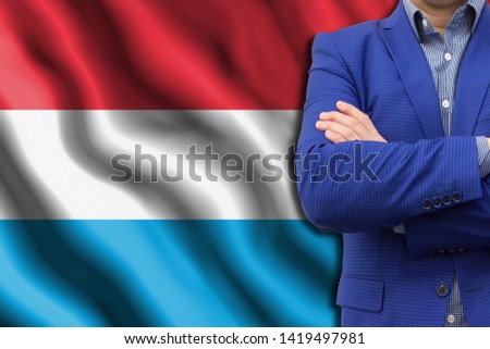 The concept of business, government, power. The elite of the country. Copy space or text. Man in blue suit close-up against the background of the developing flag of Luxembourg.