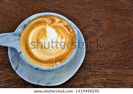 Close-up of a coffee cup that on top with leaf shape milk bubbles,  placed on a wooden table.