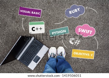 man in shoes standing on asphalt next to programming languages names and laptop