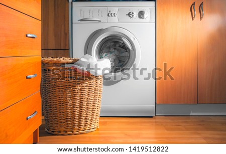 Large Wicker Laundry Basket, Lid Opened, Near the Front Load Washing Machine with Laundry. House Interior Laundry Room. Wood Interior Design. Royalty-Free Stock Photo #1419512822
