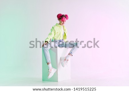 young woman with pink hair in a green jacket sits