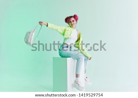 joyful woman with pink hair sits on a cube with a bag style