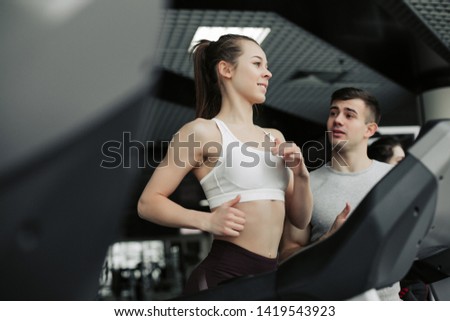 Side view of smiling sporty woman training on race track with instructions of coach. Keeping healthy lifestyle, doing cardio exercises. Girl having pretty face.
