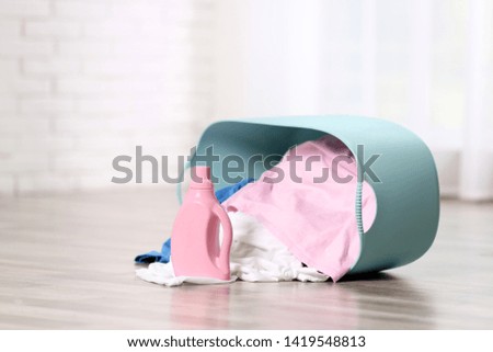 Detergent and laundry basket with dirty clothes on floor indoors. Space for text