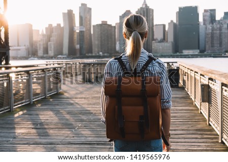 Back view of stylish female tourist with traveling backpack standing on American urban setting and examanise landmark of Manhattan district, millennial woman exploring United States during journey Royalty-Free Stock Photo #1419565976