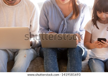 Close up of young family with preschooler kid sit on couch busy using electronic devices, modern parents and little daughter addicted to gadgets, lack real communication. Technology concept