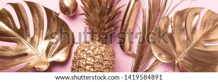 Golden exotic fruits, tropical palm, monstera leaves on pink background. Top view. Flat lay. Food concept. Creative layout of gold pineapple, banana, lemon with copy space