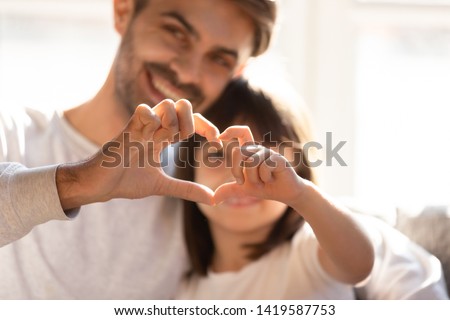 Smiling young dad and little daughter hug showing love sign express family bonding and care, happy parent embrace preschooler girl kid make hand heart gesture, enjoy tender moment together