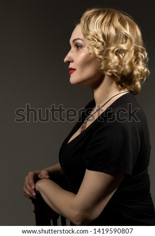 Retro portrait of beautiful woman in black dress sitting on the chair on gray background. Vintage style